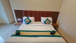 A double bed with a wooden headboard, white bedding, and two decorative pillows with a geometric pattern. - Hotel GT Galaxy (Chennai)