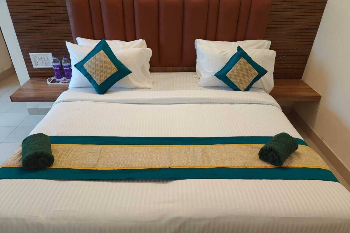 A neatly made bed with white bedding, teal and beige pillows, and a teal and beige bed runner.