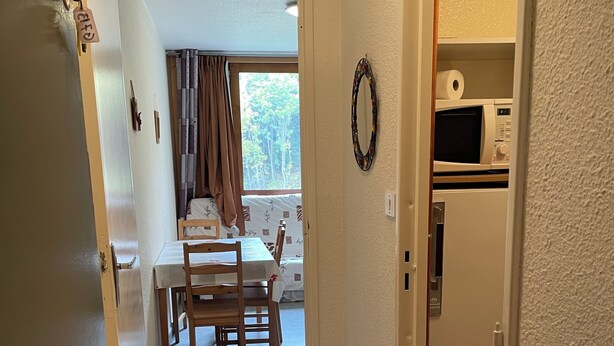 A hallway leading to a dining area with a table and chairs, a microwave, and a refrigerator.