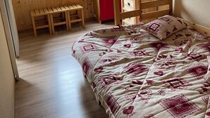 A wooden bunk bed with a patterned bedspread, a wooden bench, and a window with curtains.