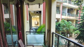 Varanda com mesa e cadeiras de vidro, um ventilador e vista para um edifício com varandas.