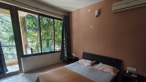 Quarto com cama, mesa de cabeceira, janela com cortinas e ar condicionado.