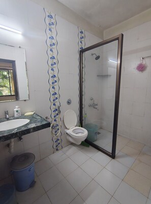A bathroom with a marble sink, a toilet with a shower enclosure, and a blue trash bin. - Tranquil 1BHK Garden Estate, Pool | Palolem Beach (Canacona)