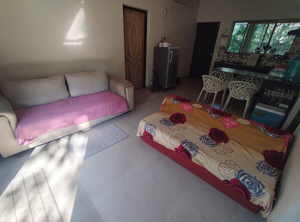 A living room with a sofa, a patterned rug, and a dining area with chairs and a table. - Tranquil 1BHK Garden Estate, Pool | Palolem Beach (Canacona)