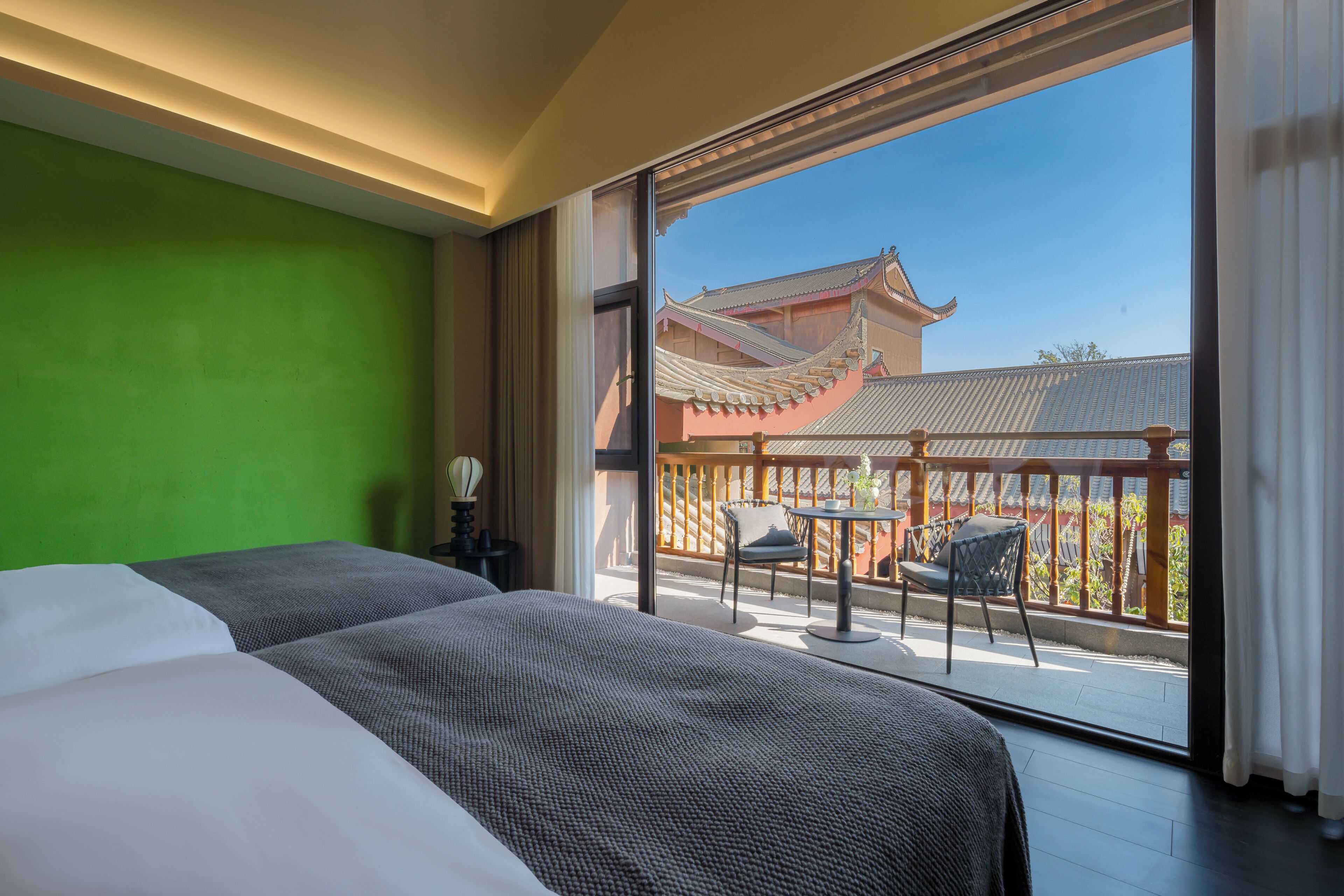 Habitación de hotel con una cama grande, una pared verde y un balcón con vistas a arquitectura tradicional.