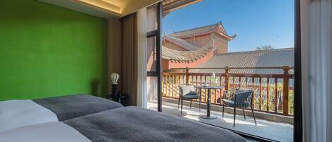 Habitación de hotel con una cama grande, una pared verde y un balcón con vistas a arquitectura tradicional.