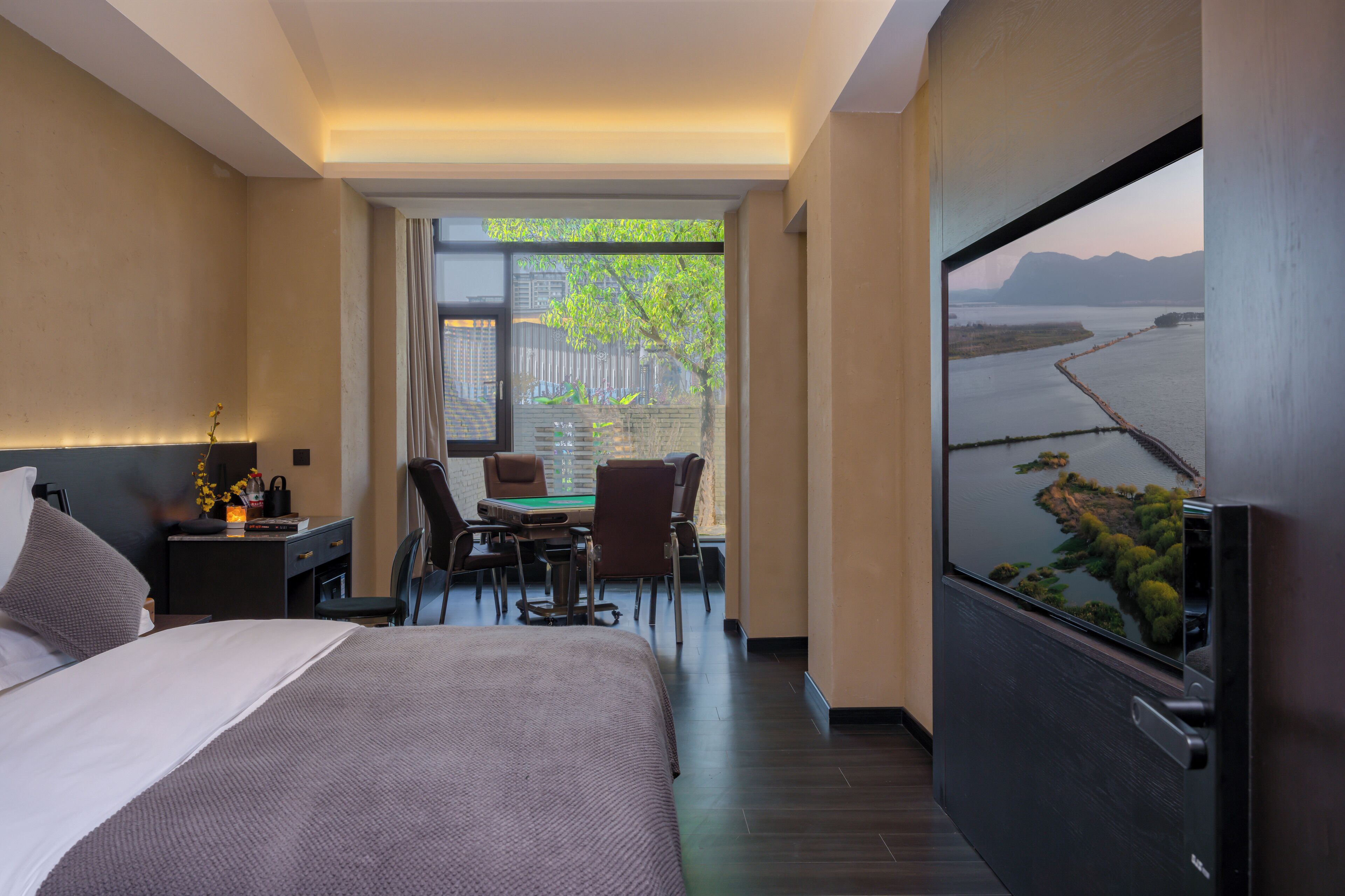 A hotel room with a bed, a desk with a chair, a TV, and a view of a body of water and greenery.