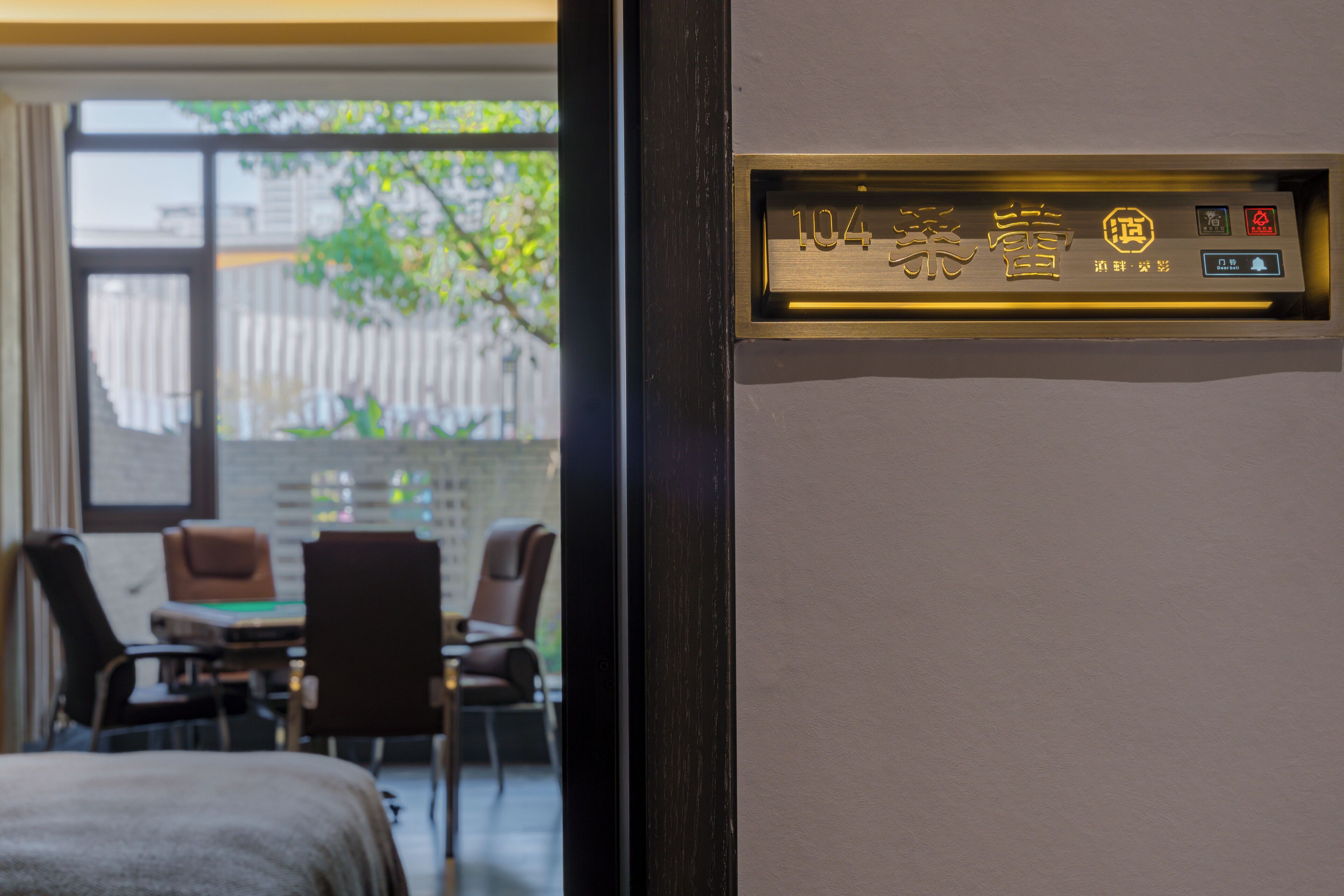 A hotel room with a wooden door, a window with a view of the outside, and a small table with chairs.
