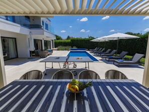 A poolside area with a table, chairs, and a fruit bowl.