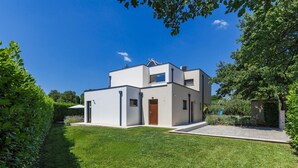 Une maison moderne à deux étages, dotée d’un toit plat, d’un petit porche à l’avant et d’une pelouse bien entretenue.