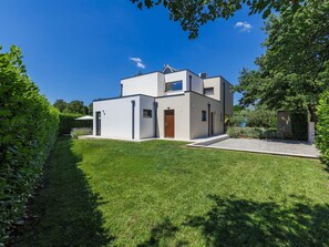Ein modernes, zweistöckiges Haus mit flachem Dach, einer kleinen Veranda und einem gepflegten Rasen.