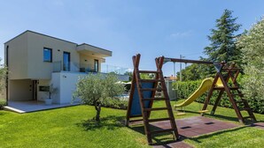 Une maison moderne à deux étages, dotée d’une pelouse bien entretenue et d’une balançoire en bois.