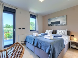 A bedroom with a bed, a chair, a painting, and a view of the outdoors.