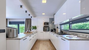 Une cuisine moderne avec des meubles blancs, un îlot central et une vue sur la verdure environnante.