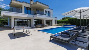 Une maison moderne à deux étages, dotée d'une piscine, d'un espace salon extérieur et d'une table de ping-pong.