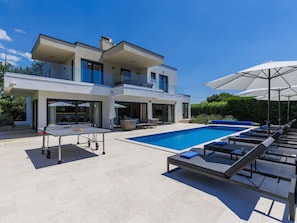 Ein modernes, zweistöckiges Haus mit Swimmingpool, Sitzgelegenheit im Freien und einem Tisch inklusive Tischtennis-Schläger.