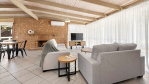 A modern living room with a brick fireplace, a flat-screen TV, and a large window with sheer curtains.