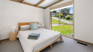 A bedroom with a large window, a bed with pillows, a bedside table with a lamp, and a view of a green landscape.
