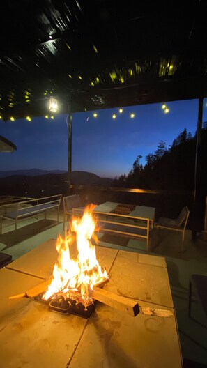 An outdoor patio with a fire feature, seating, and a view of the mountains at dusk. - Small Victories Mountain Stay (Shimla)