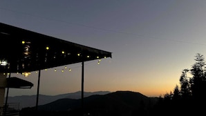 Ένας σκεπαστός εξωτερικός χώρος με φωτάκια, από τον οποίο διακρίνεται ένα ορεινό το πίο.