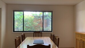 Un coin repas avec une table et des chaises, une fenêtre donnant sur un paysage verdoyant et un meuble en bois.