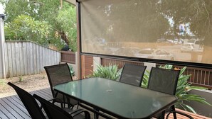 Eine Terrasse im Freien mit Tisch und Stühlen, einem Holzzaun und Blick auf parkende Autos durch ein Fenster.