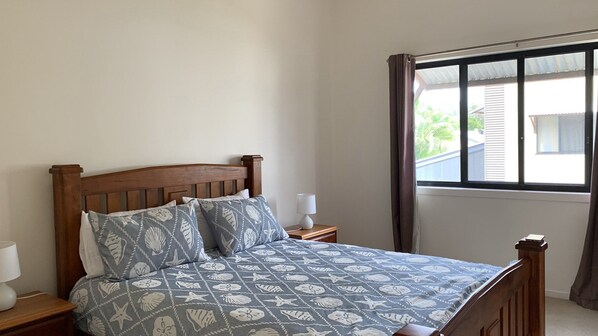 A bedroom with a wooden bed, patterned bedding, a nightstand with a lamp, and a window with curtains. - Hook Wine & Sinker by Lifestyle. Brunswick Heads (BRUNSWICK HEADS)