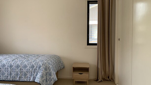 Ein Schlafzimmer mit einem Bett, einem Nachttisch, einem Fenster mit Vorhängen und einer Tür.