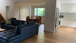 Ein modernes Wohnzimmer mit einem Ecksofa, einem Essbereich mit Holzkästen und einem Tisch sowie einer Küche mit weißen Schränken und Geräten.