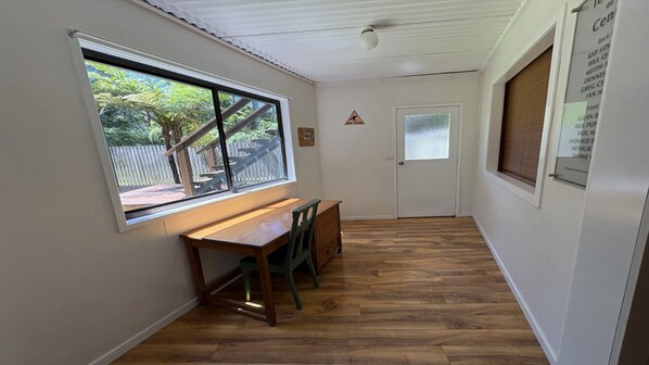A hallway with a wooden desk, a chair, and a window overlooking a fenced outdoor area.