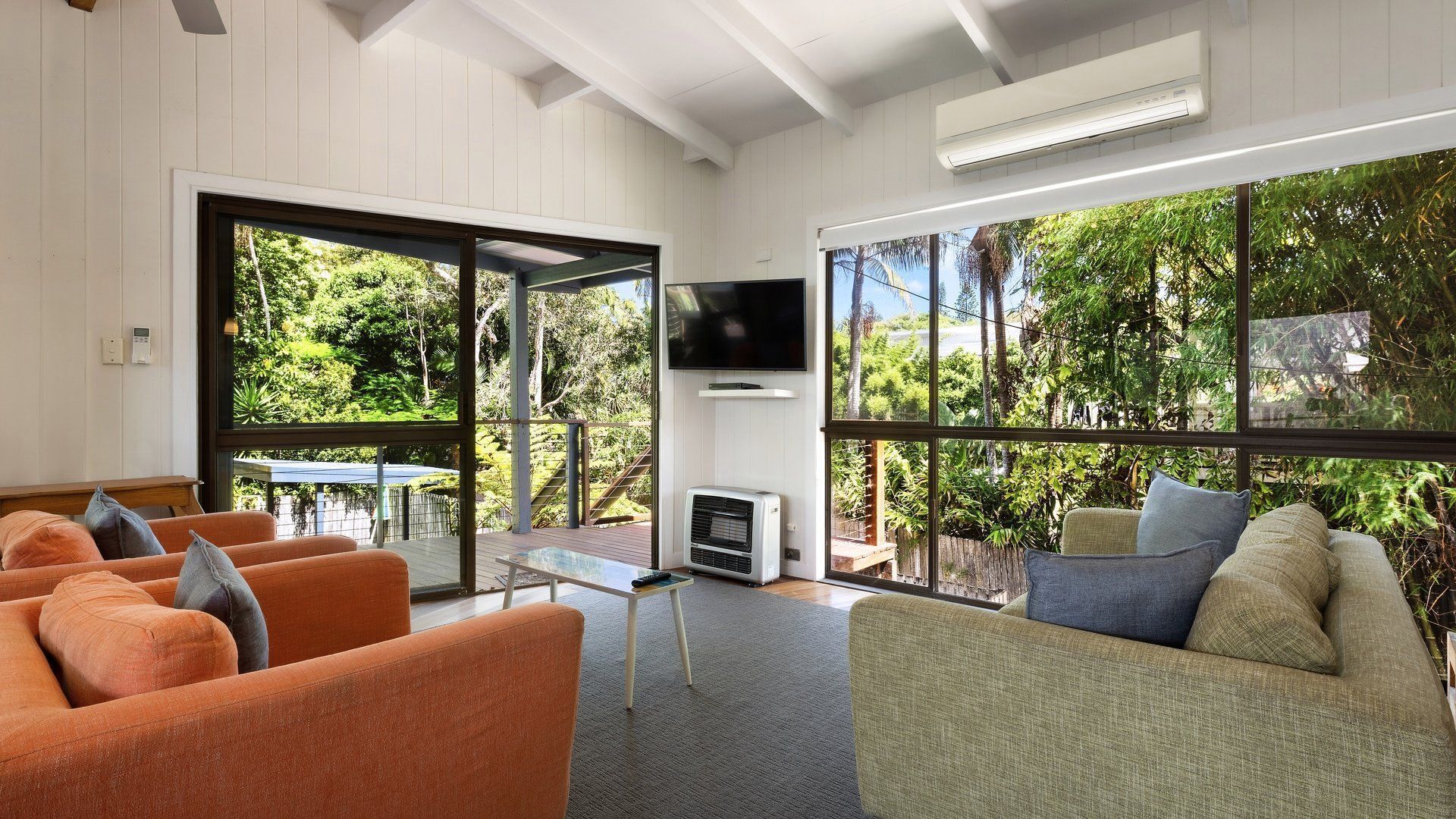 A modern living room with a TV, sofa, and large windows overlooking a garden.