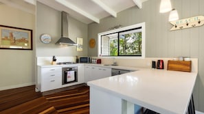 A modern kitchen with white cabinetry, a built-in oven, a microwave, and a large window with a view of greenery.