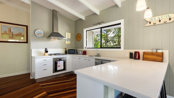 A modern kitchen with white cabinetry, a built-in oven, a microwave, and a large window with a view of greenery.