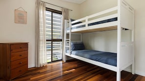 A bunk bed with a wooden dresser and a window with blinds.