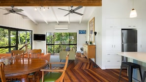 A modern kitchen with a built-in refrigerator, dining area with wooden furniture, and large windows offering a view of greenery.