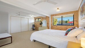 A bedroom with a large bed, a dresser, a mirror, a window with blinds, and a ceiling fan. - Seahorse On Fawcett- by Lifestyle Brunswick Heads (BRUNSWICK HEADS)