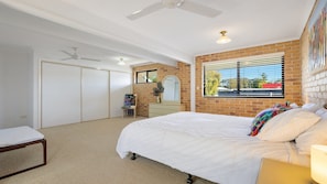 A bedroom with a large bed, a dresser, a mirror, a window with blinds, and a ceiling fan. - Seahorse On Fawcett- by Lifestyle Brunswick Heads (BRUNSWICK HEADS)