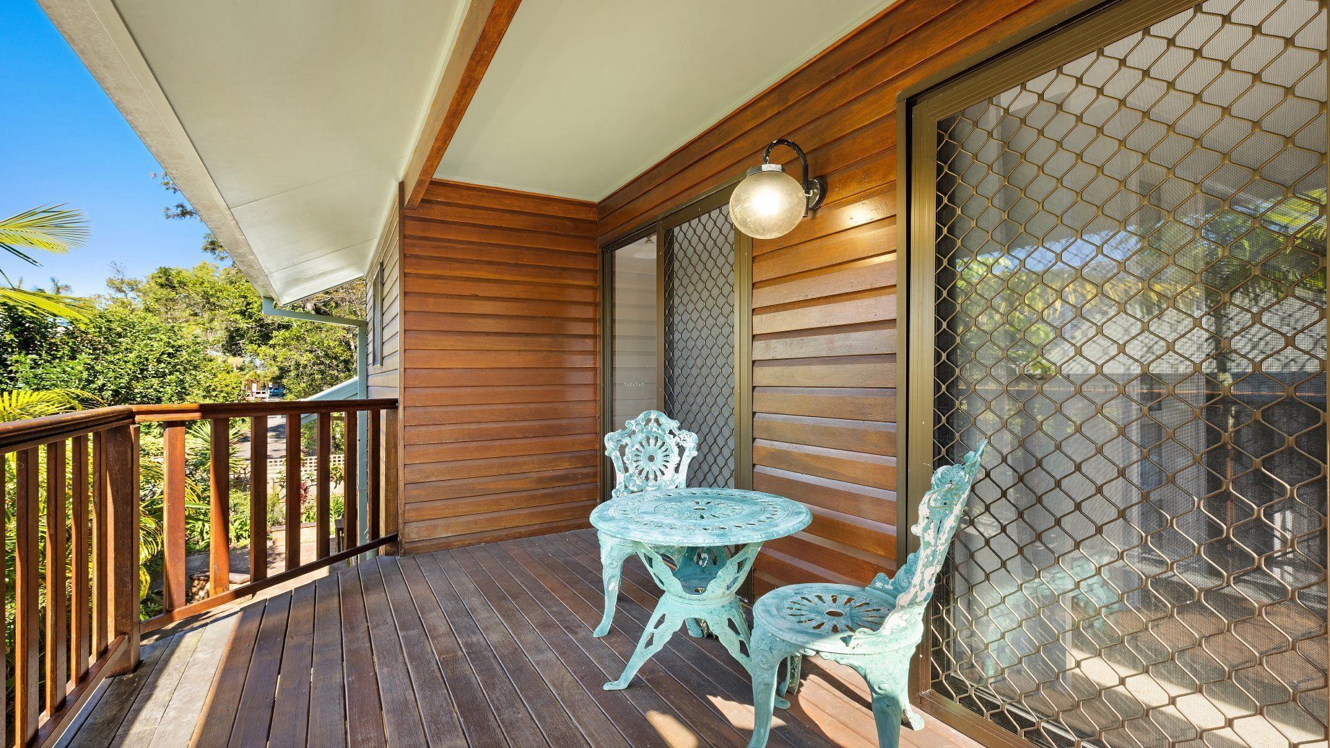 A wooden deck with a table and chairs, a covered area, and a mesh screen door.