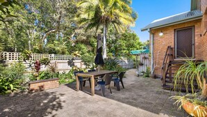 A patio area with a table and chairs, surrounded by a variety of plants and trees. - Seahorse On Fawcett- by Lifestyle Brunswick Heads (BRUNSWICK HEADS)