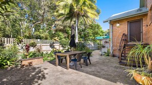 A patio area with a table and chairs, surrounded by a variety of plants and trees. - Seahorse On Fawcett- by Lifestyle Brunswick Heads (BRUNSWICK HEADS)