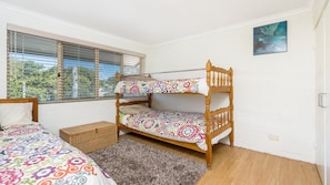 A bedroom with a bunk bed, a single bed, a wicker basket, a rug, and a painting on the wall.