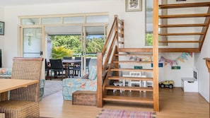 A spacious room with a wooden staircase, a dining area with wicker furniture, and a view through large glass doors.
