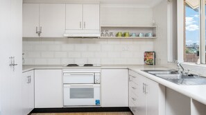 A compact kitchen with white cabinetry, a built-in oven, a stovetop, and a window providing a view of the outdoors.
