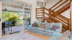 Ein Zimmer mit einer Holztreppe, einem blumigen Sofa und Blick auf Grün.