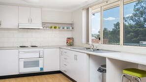 A kitchen with white cabinets, a built-in oven, a sink, and a window with a view of trees.