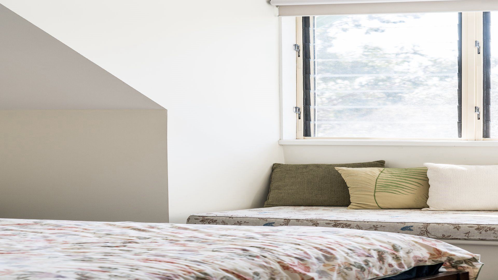 A bedroom with a bed, a window with blinds, and a view of trees outside.