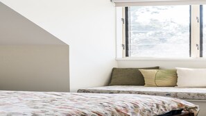 Ein Schlafzimmer mit einem Bett, einem Fenster mit Jalousien und Blick auf Bäume.