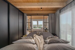 Ein modernes Schlafzimmer mit einem großen Bett, Blick ins Freie und einer Holzbalkendecke.