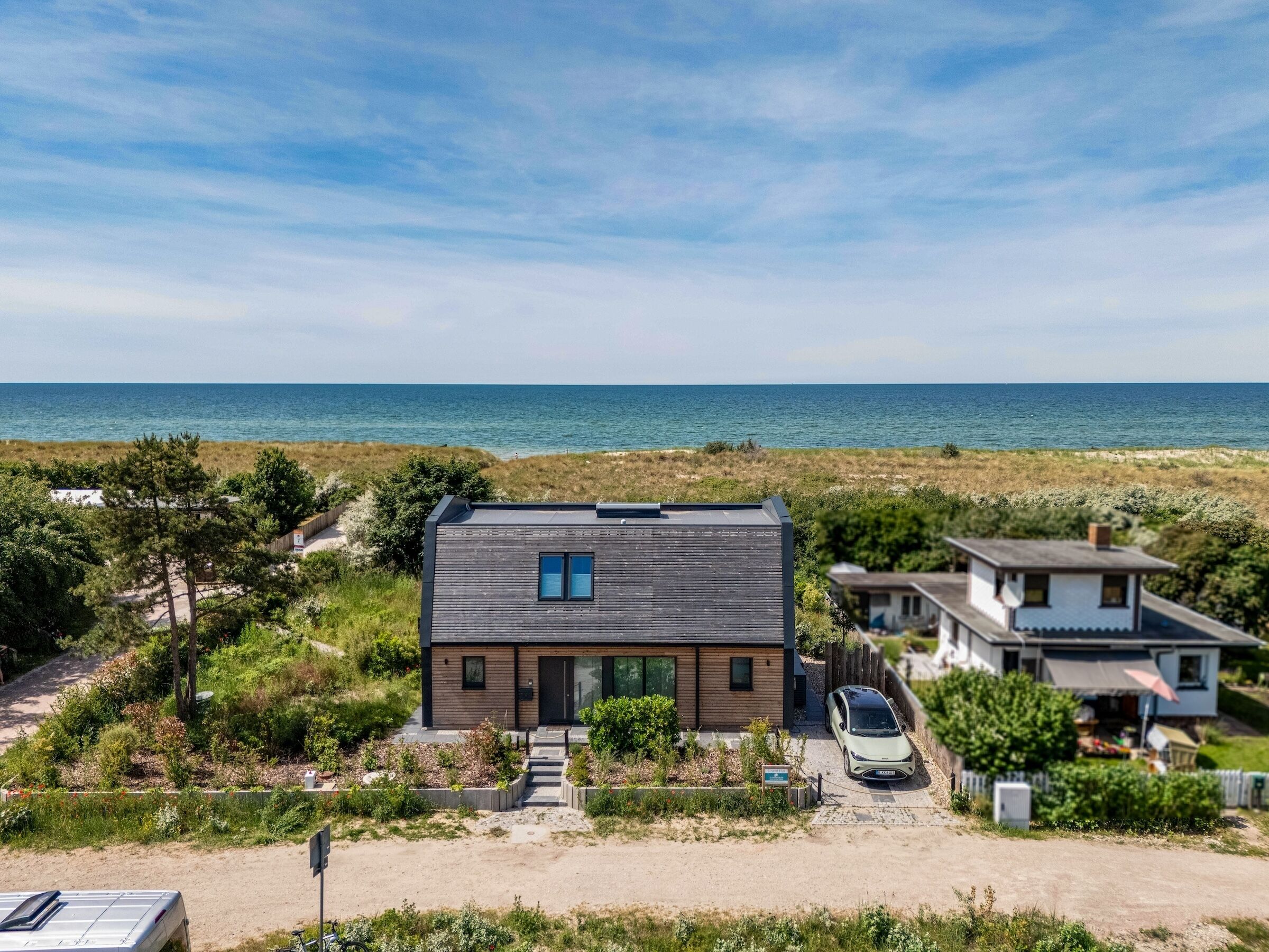 A modern house with a carport, a view of the sea, and a sandy driveway.