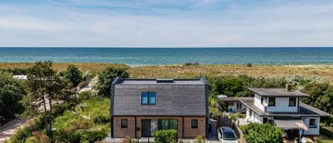 A modern house with a carport, a view of the sea, and a sandy driveway.